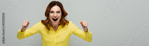 excited woman showing success gesture while standing with open mouth isolated on grey, banner
