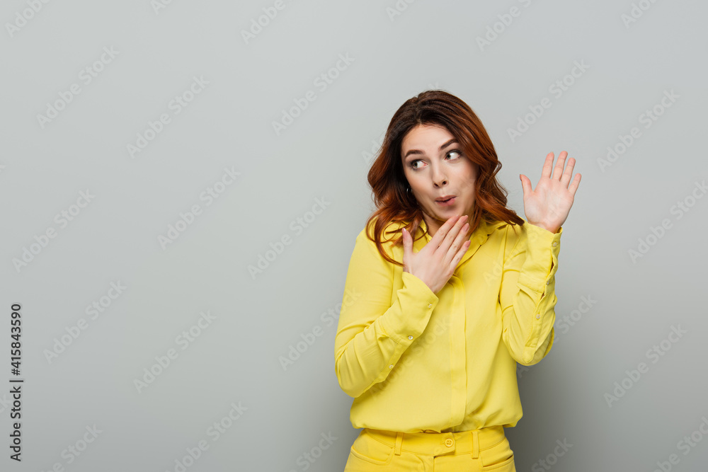 confused woman pointing with hands while looking away on grey