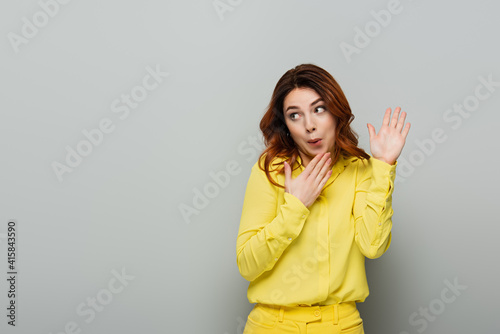 confused woman pointing with hands while looking away on grey