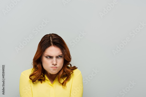 irritated woman puffing cheeks while looking away on grey