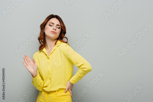 Fototapeta smug woman showing refuse gesture while standing with hand on hip on grey