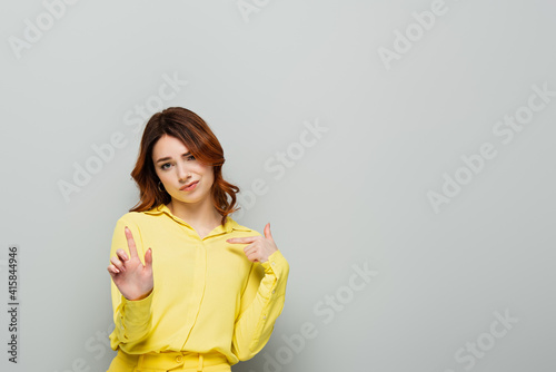 Canvas Print haughty woman pointing with finger at herself while showing stop gesture on grey