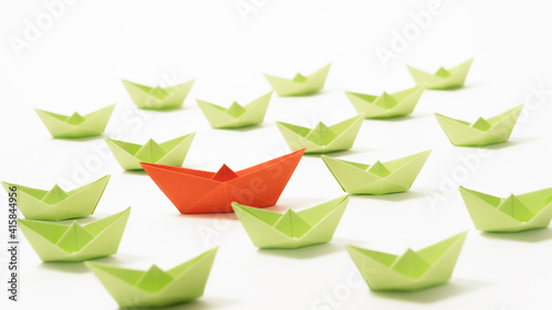 Fototapeta Naklejka Na Ścianę i Meble -  Orange paper boat among of a group of green paper boats on white background. Concept of leadership, individuality, unique.
