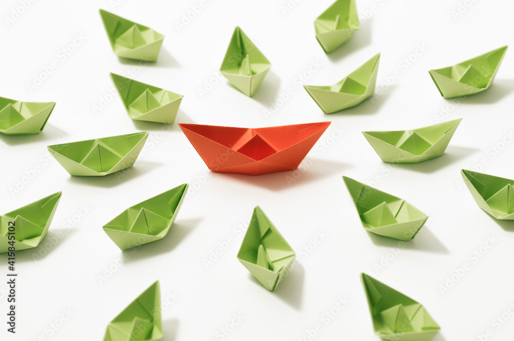 Orange paper boat among of a group of green paper boats on white background. Concept of leadership, individuality, unique. Orange paper boat among of a group of green paper boats on white background. Concept of leadership, individuality, unique.