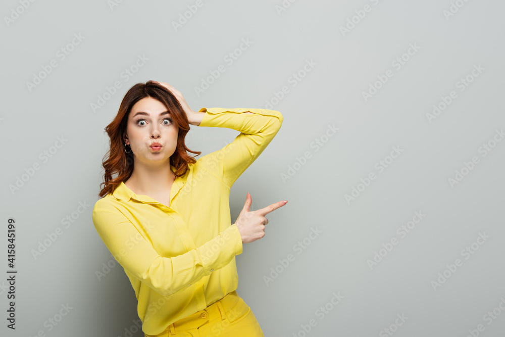 astonished woman puffing cheeks while pointing with finger on grey astonished woman puffing cheeks while pointing with finger on grey