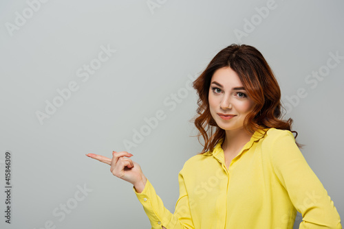 smirking woman looking at camera while pointing with finger on grey