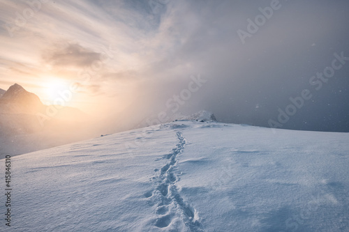 Sunrise on snowy mountain with footprint in blizzard at Senja Island