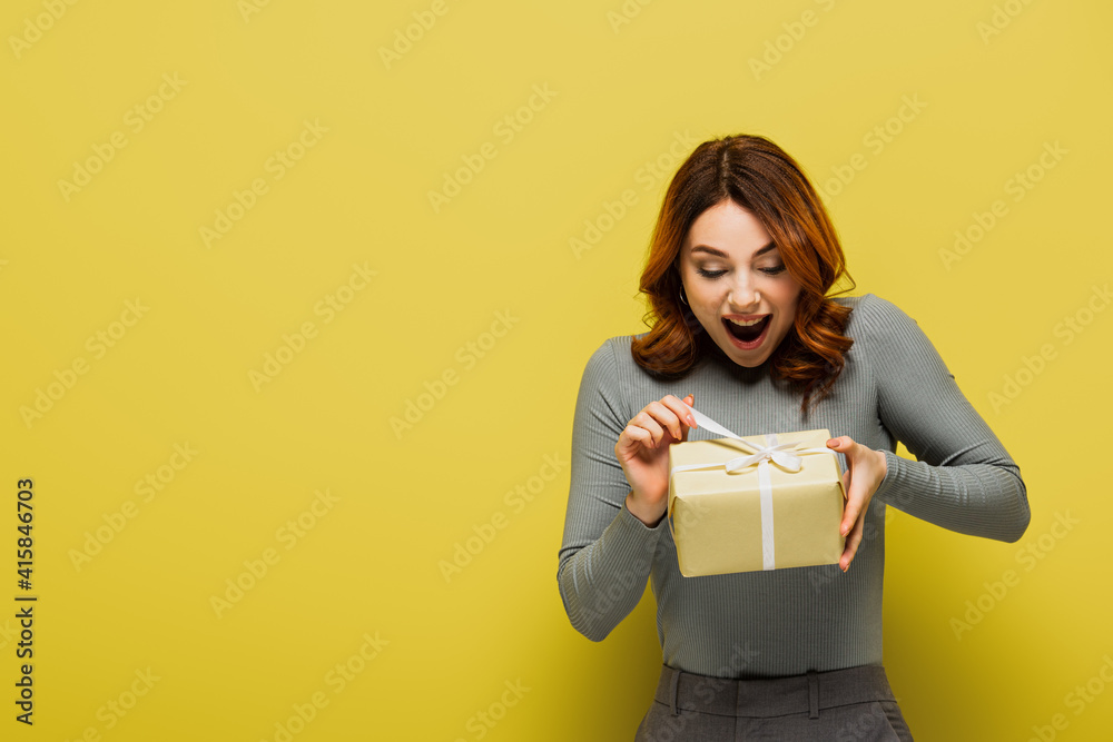 amazed young woman pulling ribbon on present on yellow amazed young woman pulling ribbon on present on yellow