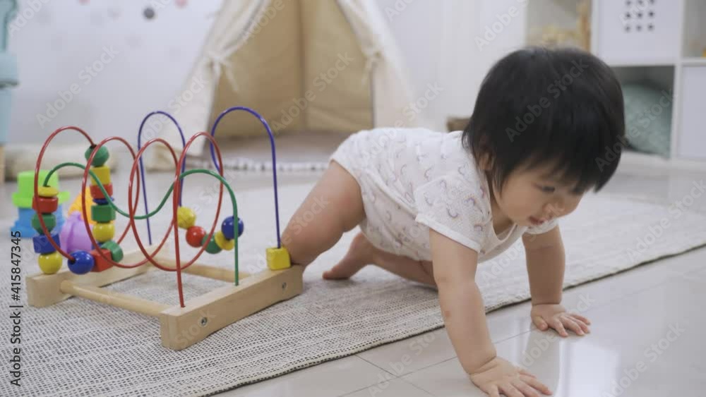 adorable asian baby is smiling at the camera innocently and crawling away from the toys on the rug in a modern cozy playroom at home. adorable asian baby is smiling at the camera innocently and crawling away from the toys on the rug in a modern cozy playroom at home.
