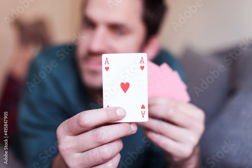 Man is showing a hearts card, playing cards, lying on a couch at home