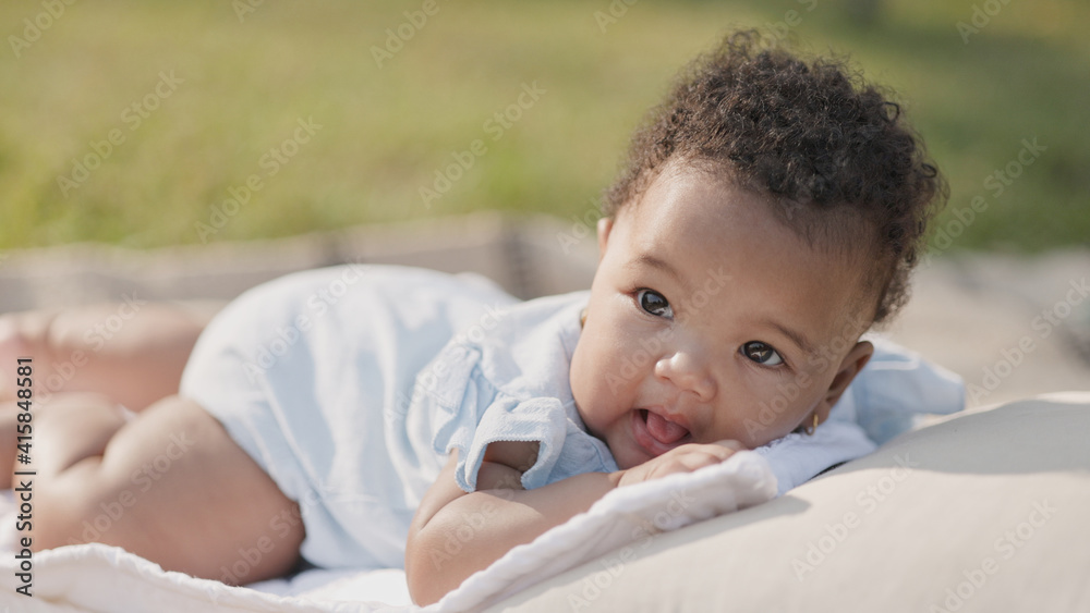 Smiling African American baby happy on mat in garden nature morning with family on vacation. Baby health care. Child development. Universal Children's Day Smiling African American baby happy on mat in garden nature morning with family on vacation. Baby health care. Child development. Universal Children's Day