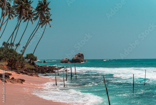 Tropikalna plaża z palmami, niebieski ocean z falami oraz kije rybackie. photo