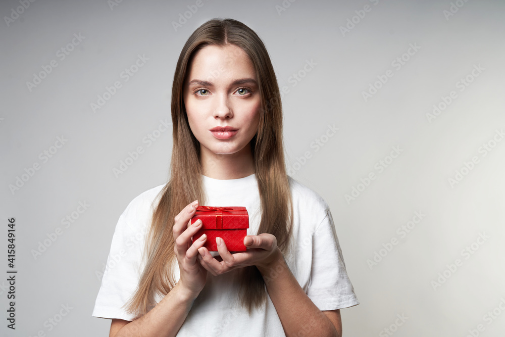 Beautiful young blonde woman on a gray background with a red small gift in hands Beautiful young blonde woman on a gray background with a red small gift in hands