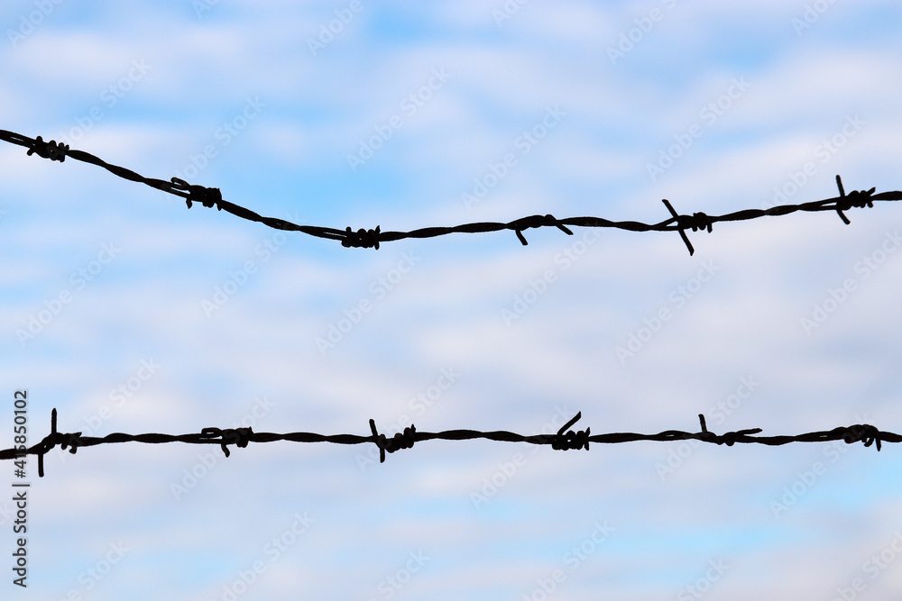 Silhouette of rusty barbed wire against the blue sky and white clouds Silhouette of rusty barbed wire against the blue sky and white clouds