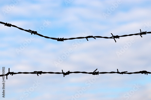 Silhouette of rusty barbed wire against the blue sky and white clouds