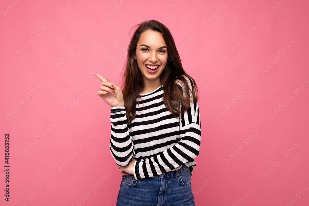 Portrait of beautiful fascinating emotional positive joyful happpy female promoter pointing to the side at copy space for advertising wearing hipster outfit isolated over background wall with empty