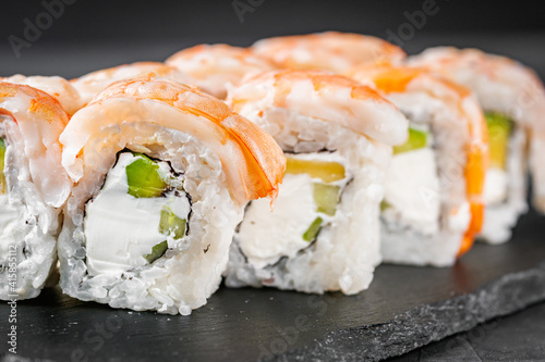 appetizing sushi roll philadelphia with avocado cheese cucumber and shrimp on a black stone plate