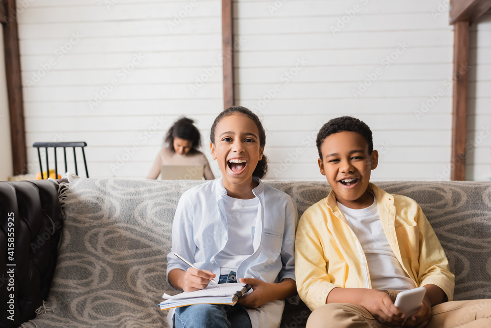 excited african american kids near mother working on blurred background excited african american kids near mother working on blurred background