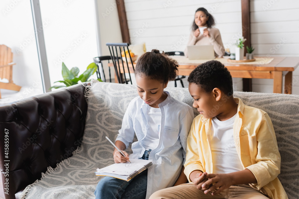 Fototapeta premium african american kids doing homework on sofa near mother