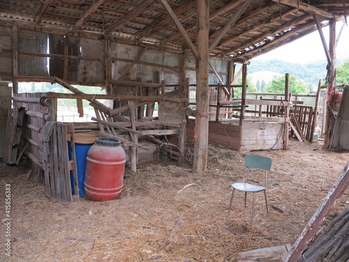Farm Grounds with Wooden Structure, Blue and Red Plastic Barrels and Green Chair in Italy © Monica