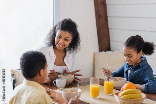 happy african american woman talking to children during breakfast