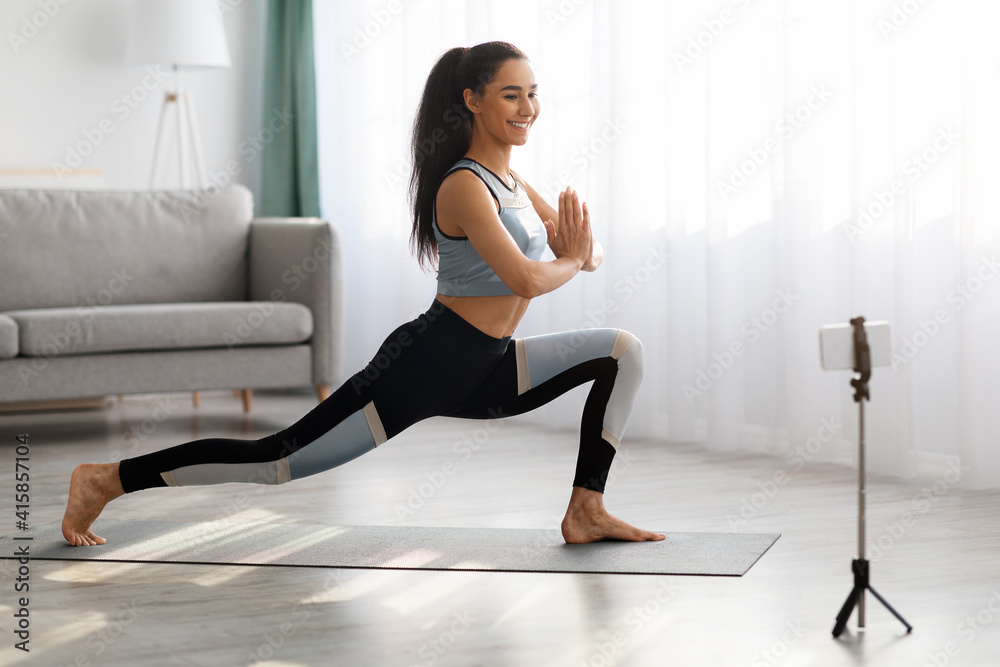 Positive young lady watching online yoga class, using smartpohne