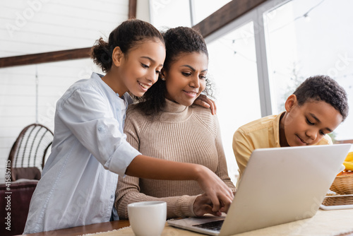 african american girl embracing mother working on laptop at home