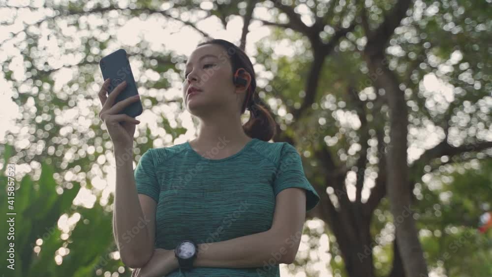 asian athlete woman wearing headphone and using mobile smart phone when jogging in green nature park in evening sunset. female in sportswear using online application tracking activity and music. asian athlete woman wearing headphone and using mobile smart phone when jogging in green nature park in evening sunset. female in sportswear using online application tracking activity and music.