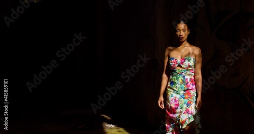 Amazing model walks out from the darkness into the direct sunlight in a long sexy dress photo