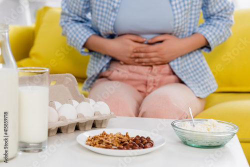 Cropped view of milk, eggs, cottage cheese and nuts near woman with allergy on blurred background