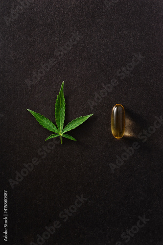 Medicinal cannabis leaf with marijuana oil in capsules on black background.