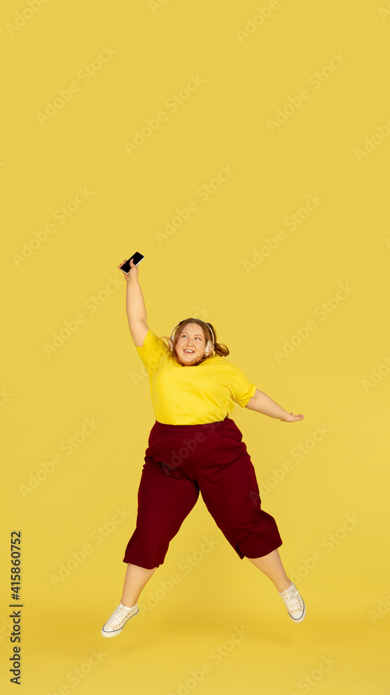 Jumping high. Beautiful plump caucasian plus size model isolated on yellow studio background. Concept of inclusion, human emotions, facial expression, sales, body positive. Copyspace for ad.