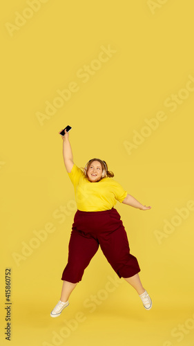 Jumping high. Beautiful plump caucasian plus size model isolated on yellow studio background. Concept of inclusion, human emotions, facial expression, sales, body positive. Copyspace for ad. © master1305