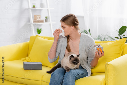 Woman with allergy holding pills and napkin near furry siamese cat on yellow sofa © LIGHTFIELD STUDIOS