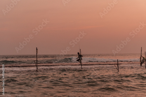 Tradycyjni rybacy wędkarze podczas połowy na palach w oceanie, na tle zachodzącego słońca.