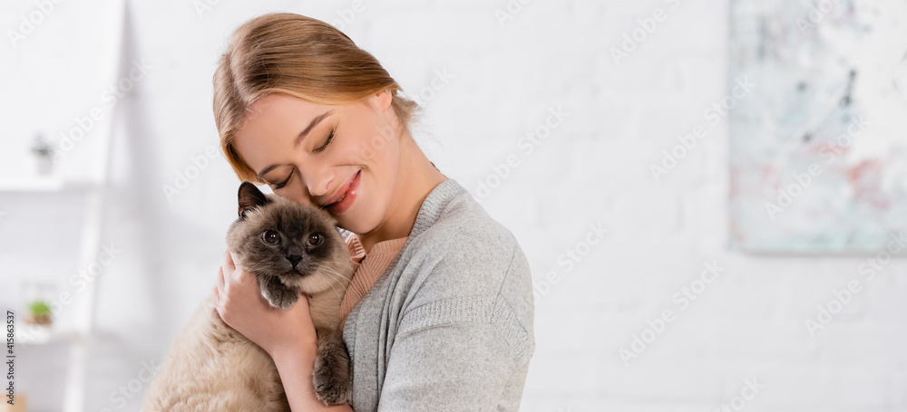 Cheerful woman with closed eyes embracing siamese cat, banner