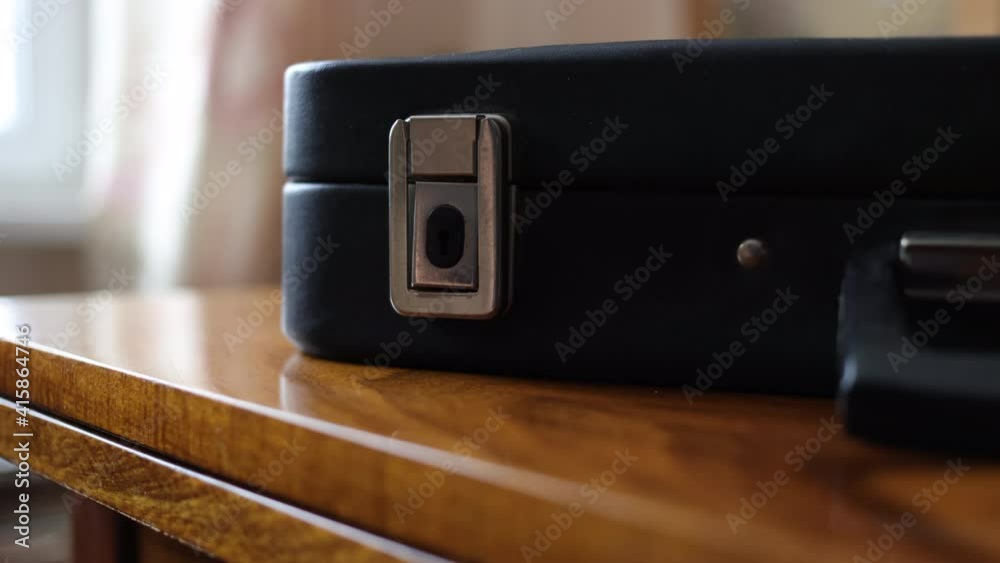 A Man Closes An Old Business Suitcase. A Black Vintage Briefcase Is Lying On A Wooden Table Near Window. A Man Closes An Old Business Suitcase. A Black Vintage Briefcase Is Lying On A Wooden Table Near Window.