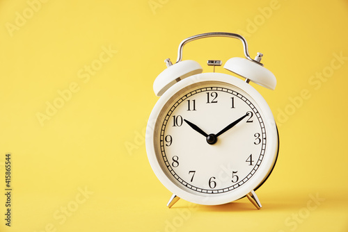 White vintage alarm clock on a yellow background with copy space