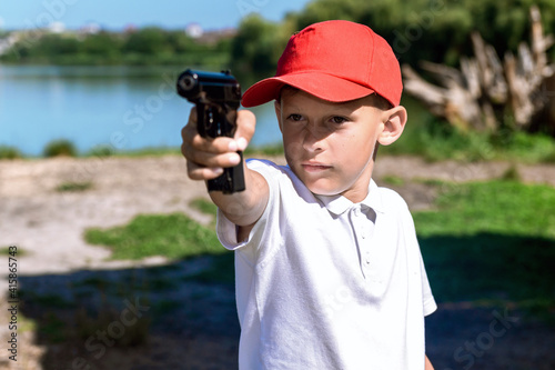 Boy shoots from a gun. Boy with a weapon near a lake.