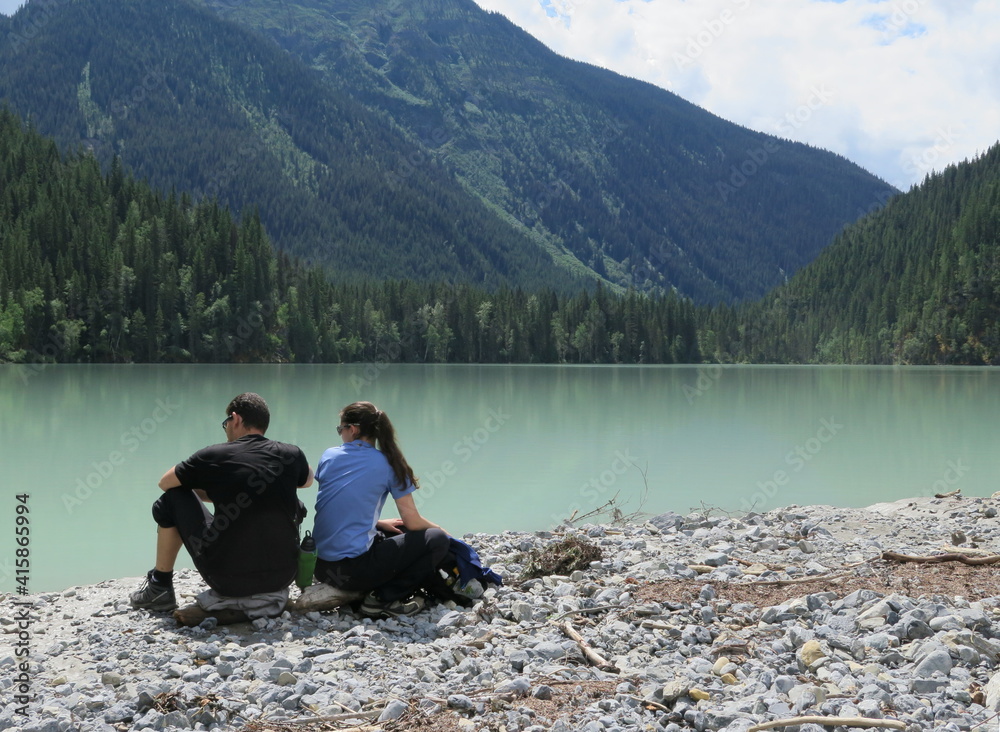 a couple sitting by the Kinney Lake, Mount Robson Provincial Park, Rocky Mountains, Alberta, Canada, July