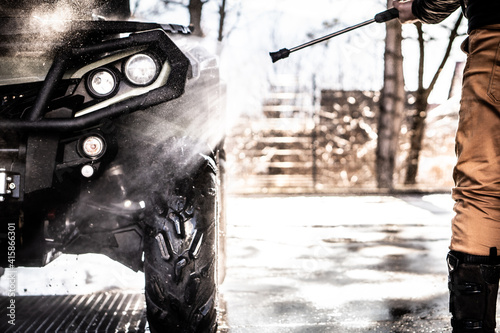 A young man is washing his dirty ATV on the car wash.