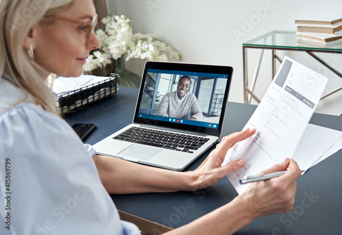 Female hr reading cv during online virtual job interview by video call. Employer checking african male recruit resume talking by distance remote recruitment chat meeting video conference on laptop.