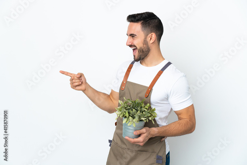 Gardener man holding a plant isolated on white background pointing finger to the side and presenting a product