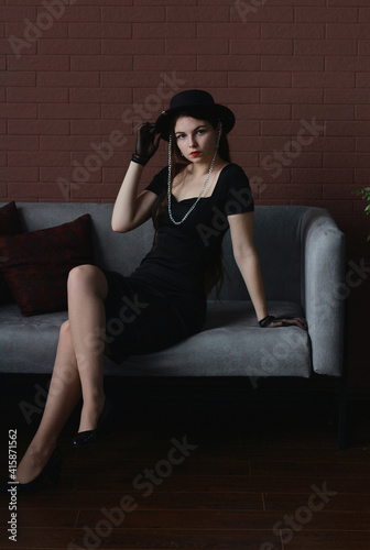 Beautiful slender brunette girl in a black dress and hat. © Valentinka