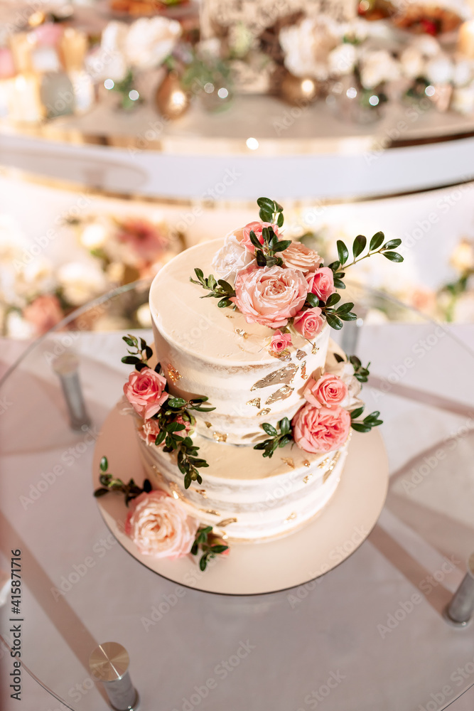 The wedding cake. White, two-tiered, decorated with flowers and gold. On a delicate pink background. Side view, top. The wedding cake. White, two-tiered, decorated with flowers and gold. On a delicate pink background. Side view, top.
