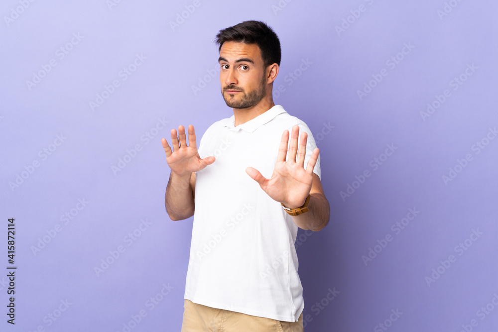 Young handsome man isolated on purple background nervous stretching hands to the front