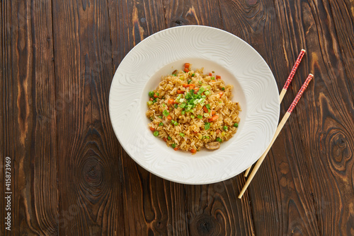 Fried rice with vegetables and beef in white plate, chopsticks on wooden background, Asian food concept, top view copy space