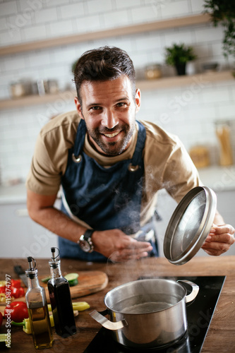  Young man cooking in the kitchen. Happy man preparing delicious food at home..