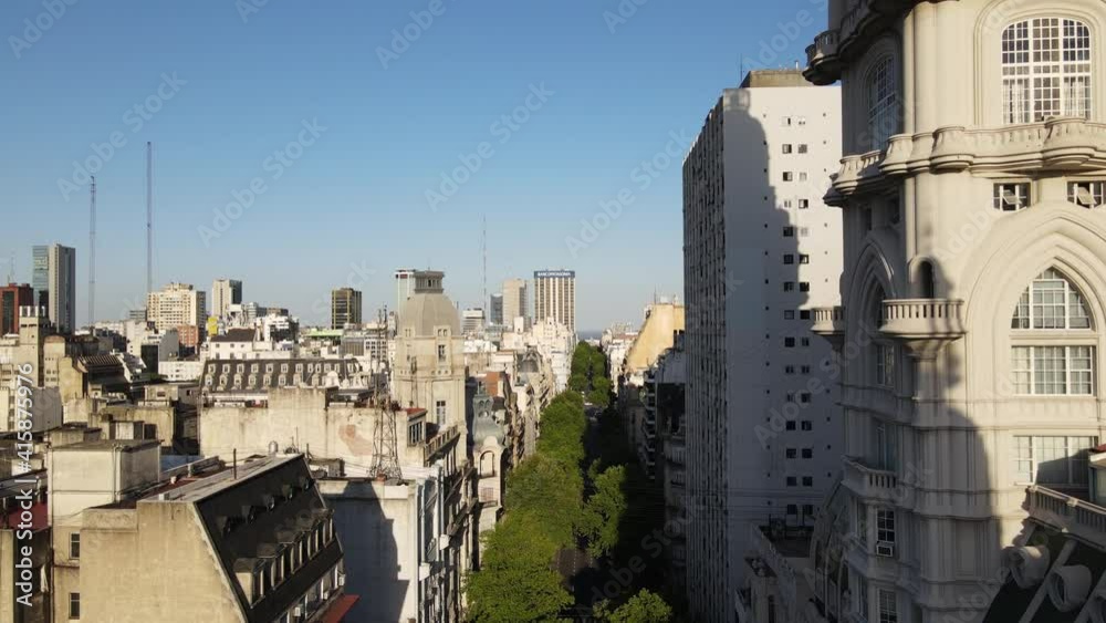 Aerial dolly out revealing Barolo Palace Tower in Avenida de Mayo with trees surrounded by Buenos Aires buildings at sunset