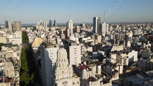 Aerial lowering on Barolo Palace tower in tree-lined May Avenue surrounded by Buenos Aires buildings at golden hour photo
